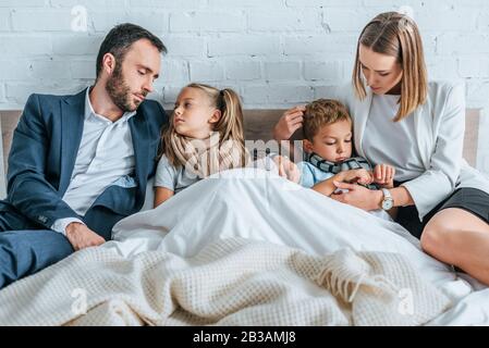 man and woman in formal wear lying in bed near sick children Stock Photo