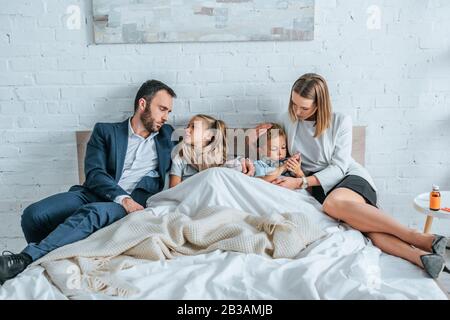 man and woman in formal wear lying in bed near diseased children Stock Photo