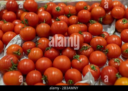Small red cherry tomatoes with a leaf, top view. Pile of ripe red tomatoes in a crate in a supermarket. Fresh Vegetables Department at Grocery Store Stock Photo