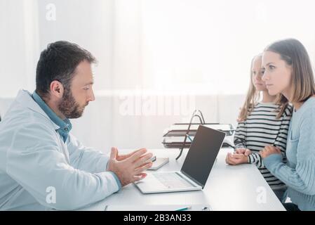 serious doctor talking to mother and daughter while sitting at table Stock Photo