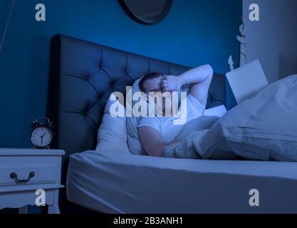 an overtired man works at late night on his laptop Stock Photo