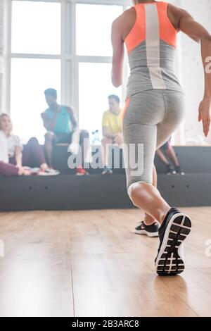 Selective focus of young woman stretching with multicultural zumba dancers at background in dance studio Stock Photo