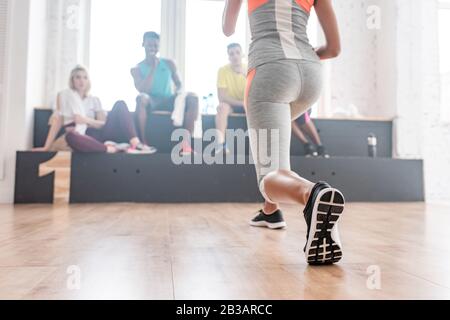 Selective focus of girl warming up with multicultural zumba dancers on bench in dance studio Stock Photo