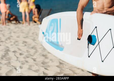 cropped view of young man holding surfing board while standing on beach Stock Photo