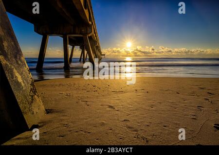 The sun rising above low level clouds illuminates the Deerfield Beach International Fishing Pier and associated shoreline Stock Photo