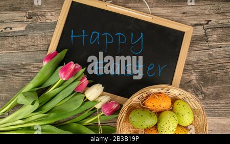 easter eggs on a wooden table with basket tulips and a blackboard Stock Photo