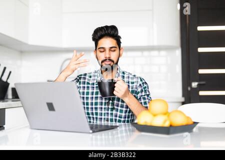 Businessman using a laptop while drinking coffee in his kitchen Stock Photo