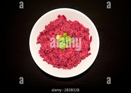 Tasty beet salad in a white bowl on a dark wooden table. Beetroot with cheese, sour cream, and green onion, healthy and fresh food.