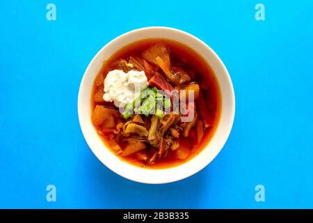 Borscht soup in a white bowl on blue background. Top view. Famous traditional Ukrainian and Russian borshch soup with beetroot and cabbage. Red Easter Stock Photo