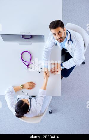 Doctors shake hands in an office in a hospital at a table with a stethoscope on a computer Stock Photo