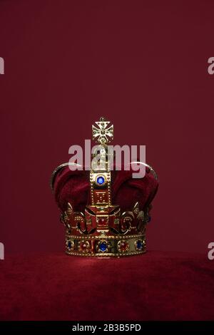 Golden crown on a velvet cushion on a deep red background with copy ...