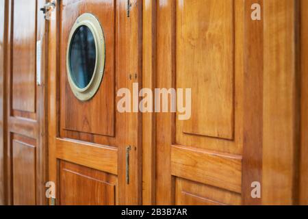 Brass porthole on varnished teak door. Detail from Norwegian Tallship Christian Radich docked in Philipsburg, Sint Maarten, Jan 2013. Select focus. Stock Photo