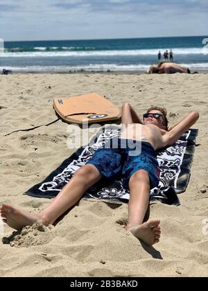 A boy lays on the beach relaxing while wearing his diabetic pump. Stock Photo