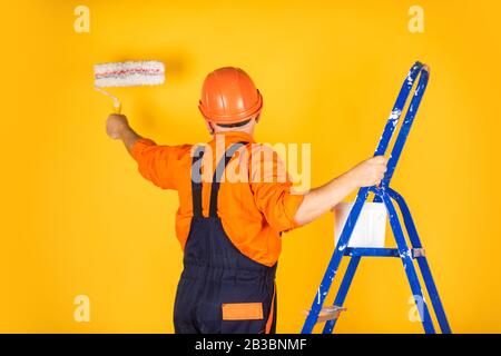 Foreman inspector. senior man painter use roller on ladder. painting the wall in yellow. professional painter in working clothes. worker painting wall in room. male decorator painting with roller. Stock Photo