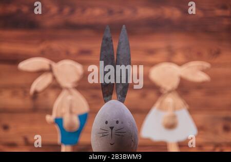 easter egg with rabbit ears in front of bunnies couple on old wood background Stock Photo