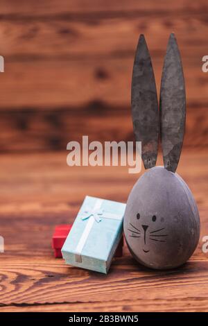 cute easter egg with bunny ears near gift boxes on wooden background Stock Photo