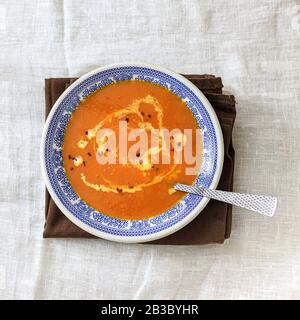 Orange pumpkin puree soup with smerana and red chili peppers in a plate with a blue traditional Moroccan pattern on a plain white background. Flat lay Stock Photo
