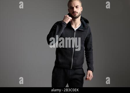 handsome casual man wearing tracksuit standing with one fist up on gray studio background Stock Photo