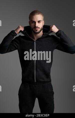 blond casual man wearing tracksuit standing and fixing his hood serious on gray studio background Stock Photo