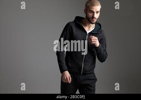 gorgeous casual man wearing tracksuit standing with loose hands and looking away serious on gray studio background Stock Photo