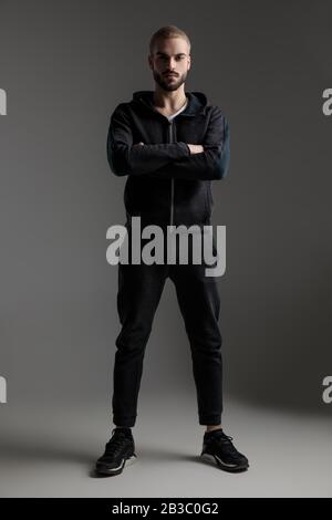 gorgeous casual man wearing tracksuit standing with crossed hands and strong posture on gray studio background Stock Photo