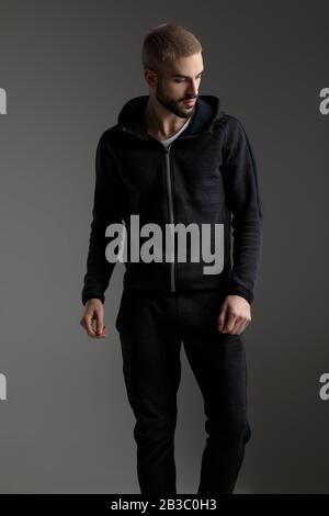 handsome casual man wearing tracksuit standing with loose hands and looking down disappointed on gray studio background Stock Photo