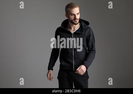 sportive casual man wearing tracksuit standing with loose hands and looking away pensive on gray studio background Stock Photo