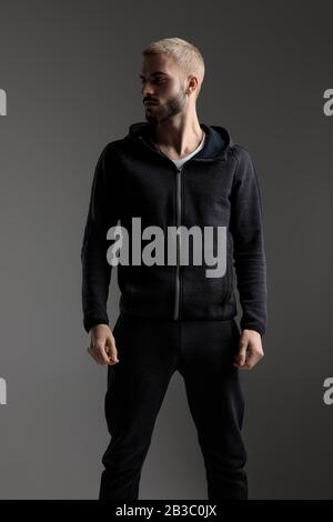 handsome casual man wearing tracksuit standing with hands loose and looking aside serious on gray studio background Stock Photo