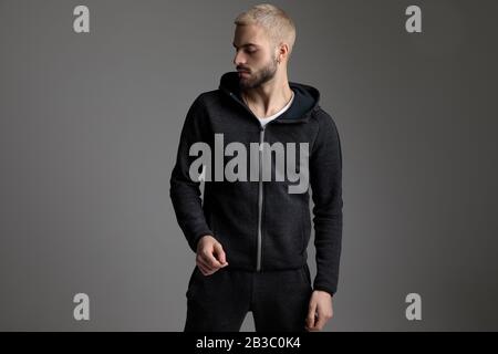 charming casual man wearing tracksuit standing and looking aside serious on gray studio background Stock Photo