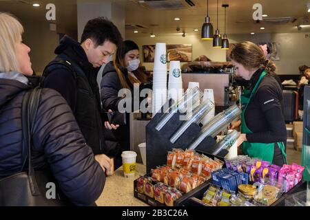 London, UK. 29th Feb 2020.  A customer, wearing a mask, buys a Starbucks Coffee at Waterloo Station as fears of the coronavirus pandemic (COVID-19) spreads across the world.   Credit Thomas Bowles alamy. Stock Photo