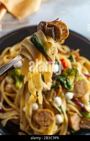 Italian chicken sausage fettuccine primavera in a garlic white wine sauce with broccoli mushrooms baby kale sundried tomatoes and tiny perline mozzare Stock Photo