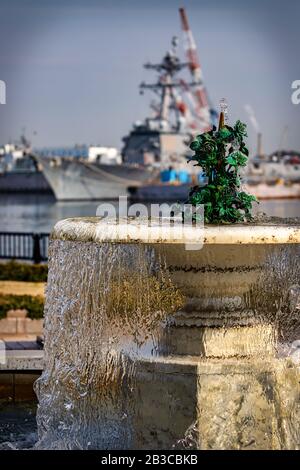 The morning sun shines on a fountain in a park with the US Navy fleet in the background at Yokosuka, Japan. Stock Photo