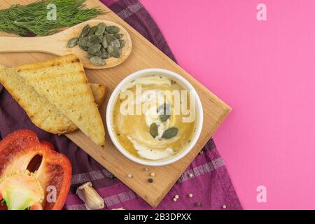 Pea soup with seeds stands on a wooden board next to croutons with mushrooms, red pepper and garlic Stock Photo
