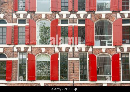 Front view of vintage windows with red wooden shutters of traditional house Stock Photo