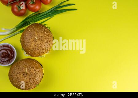 Hamburgers close-up on a yellow background, next are sauces and tomatoes with green onions Stock Photo