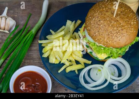 Close-up hamburger on a blue plate, next to chopped onions, french fries and ketchup Stock Photo