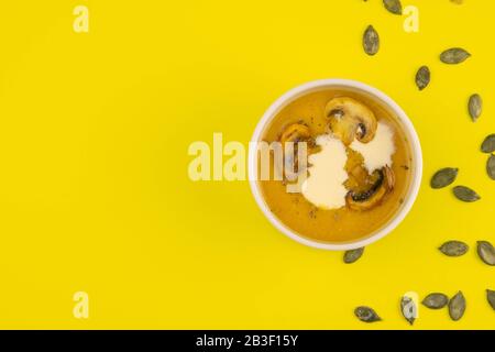 Pea soup with mushrooms in a pink plate stands on a yellow background, pumpkin seeds are scattered around Stock Photo