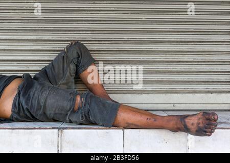 Poor homeless man or refugee sleeping on the wooden bench on the urban street in the city. Stock Photo