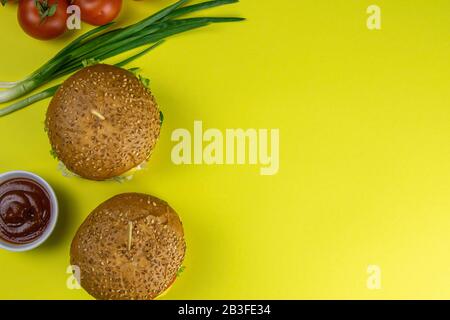 Hamburgers close-up on a yellow background, next are sauces and tomatoes with green onions Stock Photo