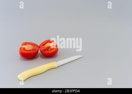 Slice tomato with yellow knife on grey background Stock Photo
