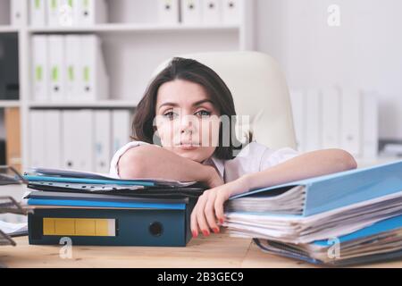 Portrait of young businesswoman exhausted with paperwork leaning on folders with work papers in office Stock Photo