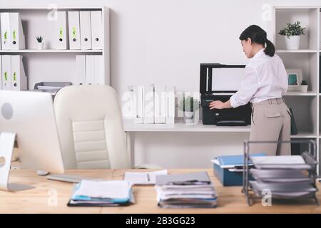 Rear view of office manager in blouse choosing amount of copies while making scan of documents on printer Stock Photo