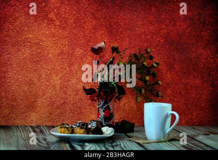 A high white mug with tea, a plate with three fresh eclairs, a vase with herbarium and a small gift box on a wooden table. Close-up. Stock Photo