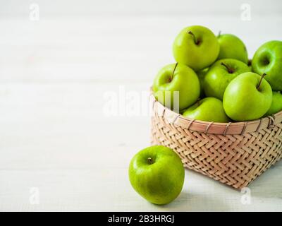 Apples harvest concept. Braided Bamboo Basket with green apples on white wooden background with copy space for text or design. Stock Photo