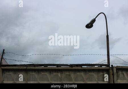 Concrete fence with barbed wire and a lantern against a cloudy sky background Stock Photo