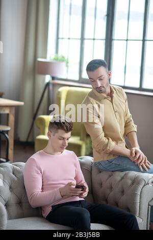 Man in orange shirt feeling jelaous watching his partner chatting online Stock Photo