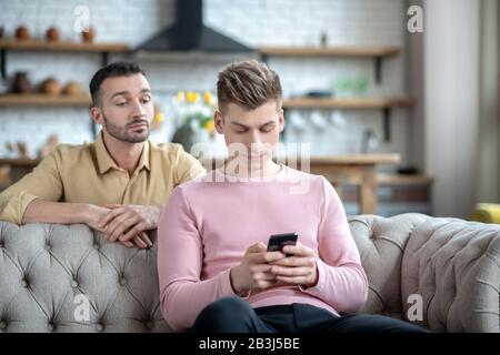 Man in orange shirt watching his partner chatting online Stock Photo