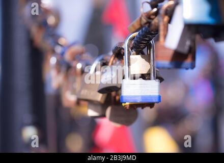 Closeup of a  blue padlock hanging on chain link of the bridge / Fence Stock Photo