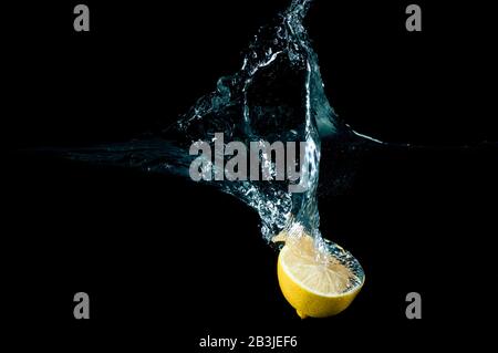 Half of a fresh lemon falling into water with splashes isolated on black background Stock Photo