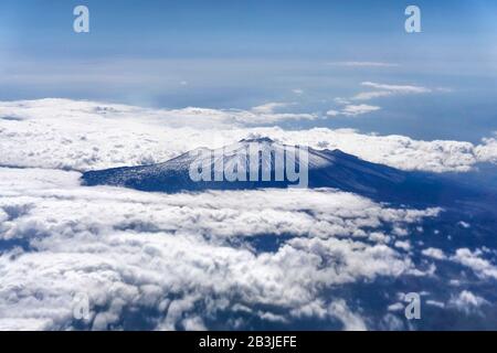 Etna volcano covered in snow. View from the plane through clouds